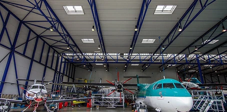 Interior of an airport hangar with several airplanes parked inside, surrounded by scaffolding and equipment for maintenance and painting.