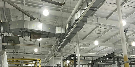 Industrial ceiling with ducts, pipes, and beams freshly painted white under bright overhead lighting.