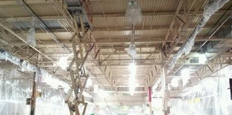 Industrial ceiling cleaning—workers using lifts to reach and clean exposed beams and fixtures in a large facility.