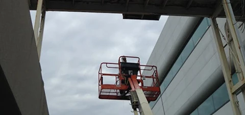 Worker on an aerial lift painting the underside of a commercial building overhang between two structures.
