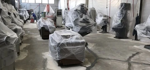 Industrial machines covered in protective plastic sheets while a workshop floor undergoes concrete polishing.