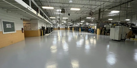 Industrial epoxy floor coatings—bright gray seamless flooring across a wide manufacturing space with equipment.