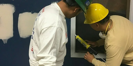 Joint sealing and caulking—workers applying sealant around a window frame to protect surfaces and joints.