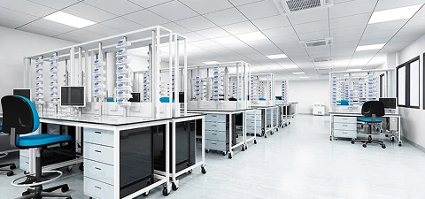 Modern pharmaceutical laboratory with bright lighting, clean white flooring, and rows of organized workstations with lab equipment.