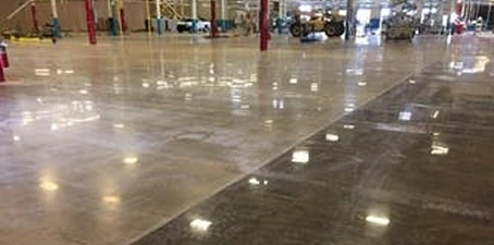 Large industrial facility floor with a smooth, glossy finish created by concrete polishing, reflecting overhead lights and machinery.