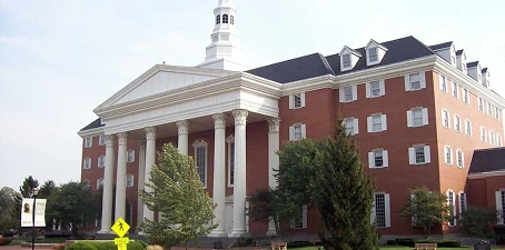 Large red-brick educational or institutional building with white columns, dormer windows, and a central clock tower against a clear sky.