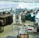 Large food and beverage processing facility with seamless, light-colored flooring, stainless steel tables, and racks filled with trays and equipment.