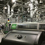 Large industrial manufacturing facility with machinery and ventilation systems, highlighting equipment cleaning and maintenance in a production environment.