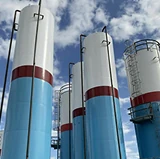 Tall industrial silos freshly painted in blue, white, and red bands, standing outdoors against a partly cloudy sky.