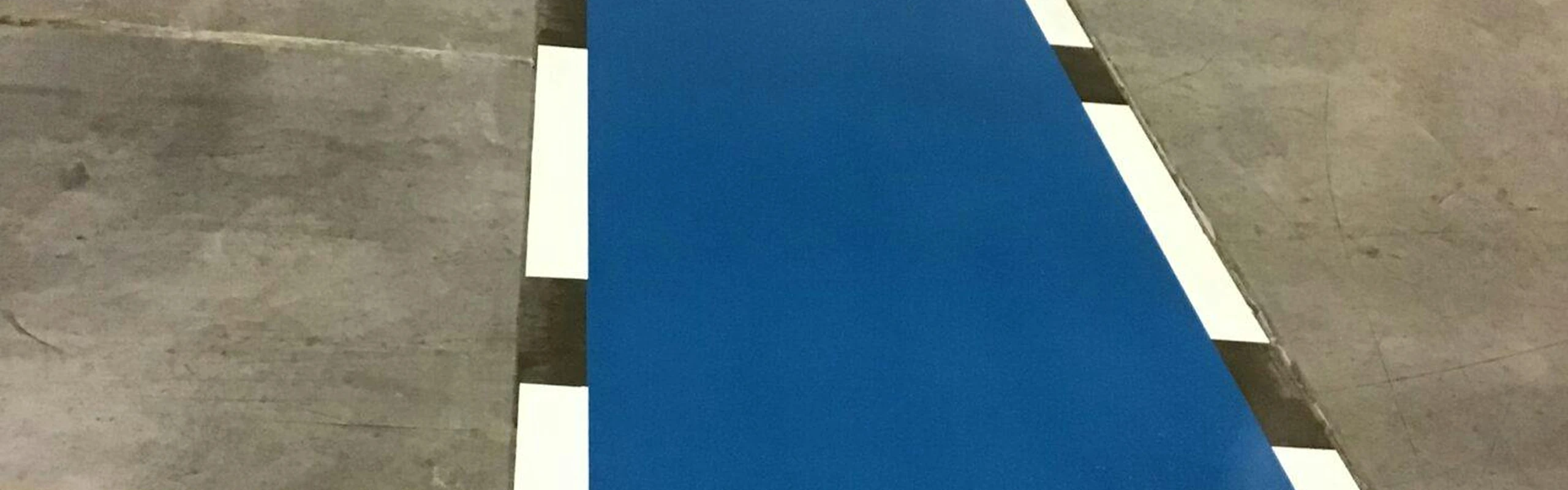 Solid blue epoxy walkway bordered by short white blocks on a gray concrete floor.